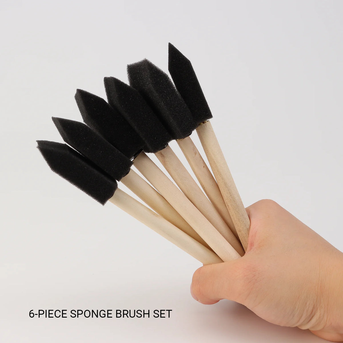 Six black foam weathering sponge brushes with wooden handles displayed in a hand